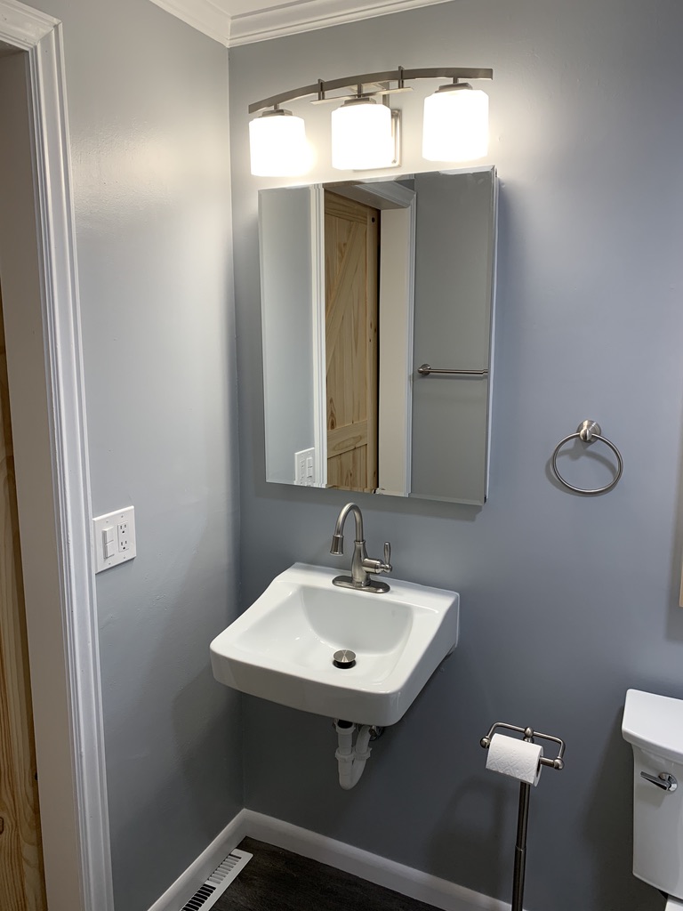 A guest bathroom with a large mirror and three overhead lights.