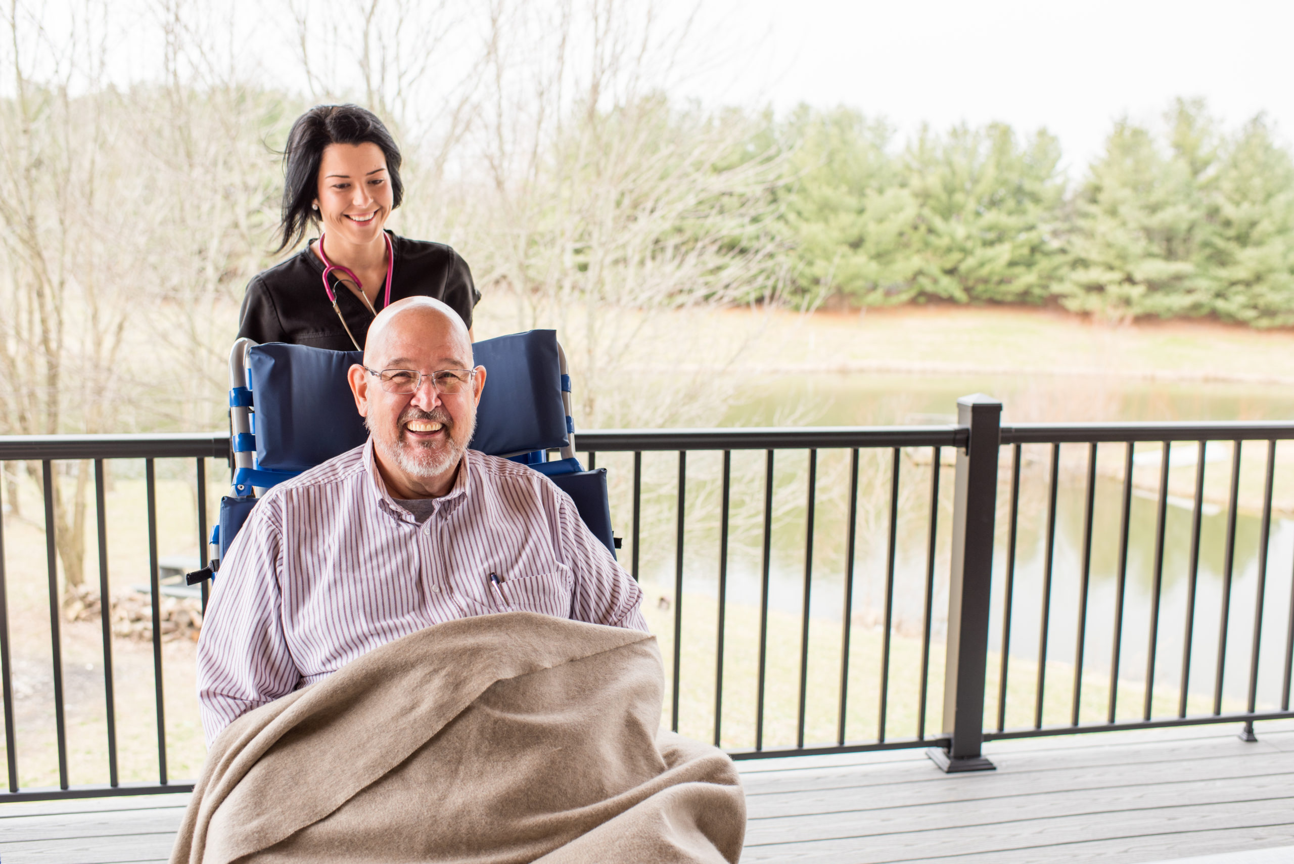 A man happily resting in a large wheelchair, covered in a blanket.