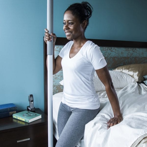 A woman using a ceiling to floor stabilizing pole to rise from bed.